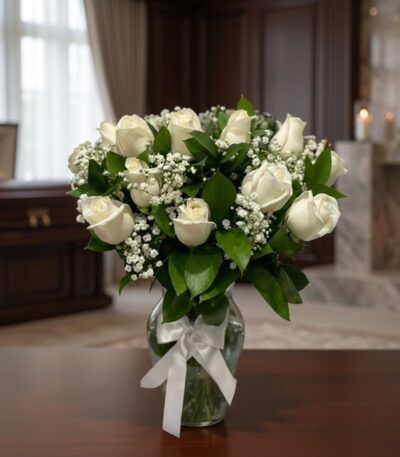 Arreglo fúnebre Pétalos del Alma con rosas blancas y follaje verde en un jarrón de cristal con lazo blanco, sobre una mesa de