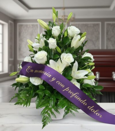 Arreglo fúnebre Piedad con rosas y lirios blancos, cinta morada con mensaje de condolencia, en sala de velación premium.