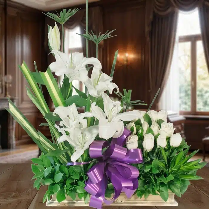 Arreglo Fúnebre Pureza: Lirios y Rosas Blancas para Homenaje Arreglo fúnebre Pureza con lirios y rosas blancas, lazo morado, en sala de velación premium con luz natural y bokeh.