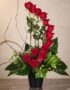 Arreglo floral GIANNA con 13 rosas rojas frescas en un jarrón negro, ramas decorativas y follaje verde, sobre una superficie