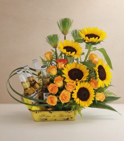 Arreglo floral vibrante con girasoles, rosas naranjas y cuatro botellas de cerveza Corona en una base amarilla, ideal para ce