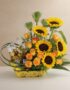 Arreglo floral vibrante con girasoles, rosas naranjas y cuatro botellas de cerveza Corona en una base amarilla, ideal para ce