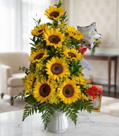 Arreglo floral premium con girasoles vibrantes y follaje verde, presentado en un jarrón blanco sobre una mesa de mármol en un