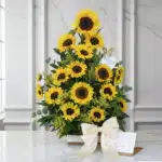 Impresionante arreglo floral con girasoles vibrantes, follaje verde y un lazo de satén, presentado sobre una mesa de mármol.