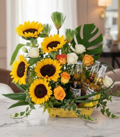 Arreglo floral vibrante con girasoles, rosas blancas y naranjas, follaje verde y tres botellas de cerveza Corona, ideal para