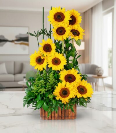 Arreglo floral con girasoles vibrantes y follaje verde en una base de madera, sobre una superficie de mármol pulido en un ent