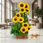 Arreglo floral 'Arreglo con Girasoles Verano' en base de madera, con girasoles vibrantes y follaje verde, sobre mesa de mármo
