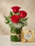 Elegante arreglo floral con tres rosas rojas vibrantes, follaje verde y flores blancas, acompañado de una caja de bombones Fe