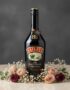 Botella de Baileys The Original Irish Cream de 700ml, rodeada por un delicado arreglo floral de rosas rosadas y burdeos, y fl