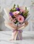 Bouquet Floral CARINA con gerberas y astromelias rosadas, lisianthus morados, envuelto en papel coreano elegante sobre mármol