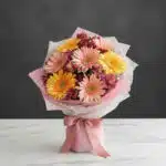 Bouquet de gerberas multicolor en tonos pastel (rosas y amarillas) con alstroemerias, envuelto en papel rosa y blanco, sobre