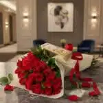 Elegante bouquet de rosas rojas frescas con bombones Ferrero Rocher sobre mesa de mármol en un lujoso recibidor.