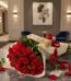 Elegante bouquet de rosas rojas frescas con bombones Ferrero Rocher sobre mesa de mármol en un lujoso recibidor.
