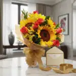 Elegante bouquet de rosas rojas y girasoles, envuelto en papel decorativo y cinta dorada, sobre mesa de mármol en un ambiente