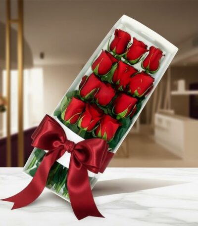 Caja de 12 rosas rojas frescas y vibrantes, presentadas en un elegante estuche blanco con un lazo de satén rojo, sobre una su