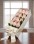 Caja blanca inclinada con 12 rosas rosadas frescas y un moño de satén, sobre una mesa de madera oscura con un fondo elegante