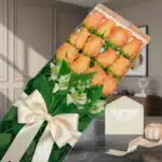 Caja de 12 rosas salmón frescas con alstroemerias blancas, lazo de satén beige, tarjeta de regalo y cinta sobre mármol oscuro