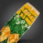 Caja de 18 rosas amarillas frescas con follaje verde y lazos dorados, ideal para regalar en cualquier ocasión especial.