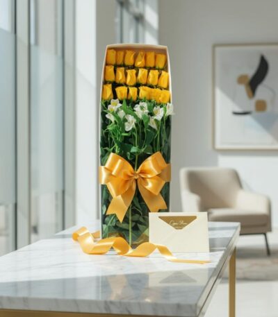 Caja de 18 rosas amarillas frescas con alstroemerias blancas, lazo dorado, tarjeta de regalo y cinta de satén sobre mesa de m