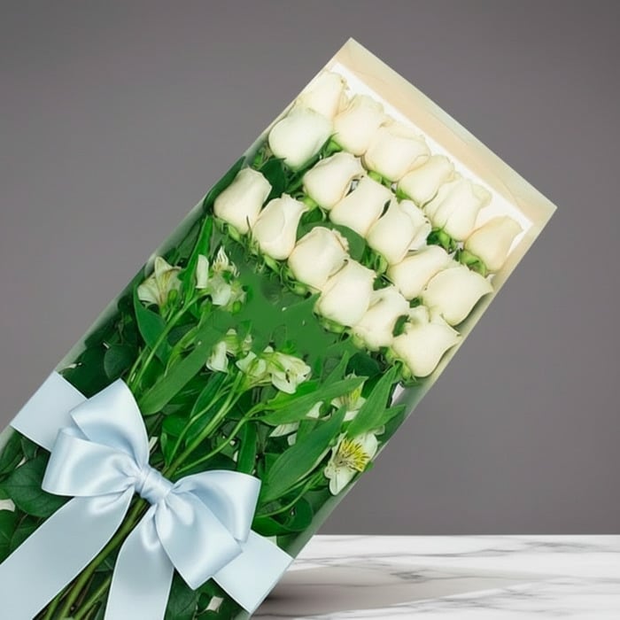 Caja de 18 rosas blancas frescas y vibrantes, con follaje verde y un lazo azul claro, sobre un fondo gris elegante. Ideal par