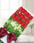 Caja de 18 rosas rojas frescas y alstroemerias blancas, con un elegante moño burdeos, sobre una mesa de mármol con fondo difu
