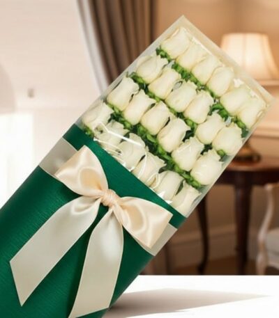 Caja de 24 rosas blancas frescas y elegantes, envueltas en papel verde oscuro con un moño de satén color crema, sobre un fond