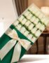 Caja de 24 rosas blancas frescas y elegantes, envueltas en papel verde oscuro con un moño de satén color crema, sobre un fond