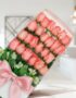 Caja de 24 rosas rosadas frescas con moño de seda rosa, dispuestas elegantemente en un fondo luminoso y moderno, ideal para e