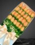 Caja premium de 24 rosas salmón frescas con follaje verde y lazo de satén, sobre fondo oscuro elegante.