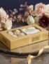 Caja de 8 chocolates Ferrero Rocher dorados sobre una bandeja de mármol con un lazo dorado y un arreglo floral elegante de fo