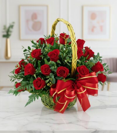 Canasta floral de mimbre verde con 24 rosas rojas vibrantes, follaje verde y un lazo rojo brillante, sobre una mesa de mármol