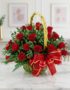 Canasta floral de mimbre verde con 24 rosas rojas vibrantes, follaje verde y un lazo rojo brillante, sobre una mesa de mármol