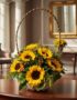 Canasta floral con 12 girasoles vibrantes y follaje verde, sobre una mesa de madera pulida en un recibidor elegante con espej