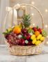 Canasta de mimbre con frutas frescas variadas como piña, uvas, manzanas, kiwis, naranjas, peras, fresas y plátanos, decorada