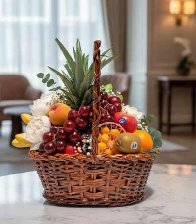 Canasta de mimbre con piña, uvas rojas, manzanas, duraznos, kiwis, naranjas y plátanos, con flores blancas y eucalipto, sobre
