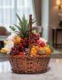 Canasta de mimbre con piña, uvas rojas, manzanas, duraznos, kiwis, naranjas y plátanos, con flores blancas y eucalipto, sobre