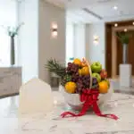 Canasta de frutas premium con piña, uvas, manzanas y naranjas, decorada con un lazo rojo y una tarjeta de regalo elegante, so