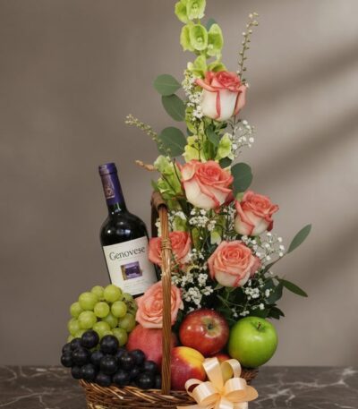 Cesta gourmet CAPRICE con rosas frescas, uvas verdes y negras, manzanas rojas y verdes, duraznos y una botella de vino tinto