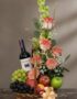 Cesta gourmet CAPRICE con rosas frescas, uvas verdes y negras, manzanas rojas y verdes, duraznos y una botella de vino tinto