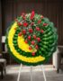 Corona fúnebre Adela con rosas rojas y flores blancas sobre base de crisantemos amarillos y hojas verdes, en sala de velación