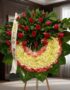 Corona fúnebre Adiós Sincero con rosas rojas y flores blancas, en una sala de velación premium con luz natural suave y bokeh.