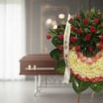 Corona fúnebre Adiós Sincero con rosas rojas y flores blancas, cinta personalizada, en sala de velación moderna con ataúd des