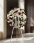Corona de homenaje fúnebre Ararat con flores blancas y rojas, lirios, rosas y margaritas, sobre un trípode en una sala de vel