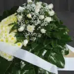 Fotografía macro premium de la Corona Fúnebre Descansa en Paz, mostrando texturas hiperrealistas de pétalos blancos y follaje