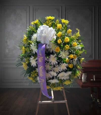 Corona fúnebre 'Estamos Contigo' con flores amarillas y blancas, cinta morada con mensaje de condolencia, junto a un ataúd en