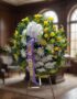 Corona fúnebre 'Estamos Contigo' con flores amarillas y blancas, lazo morado, en sala de velación premium con luz natural sua