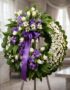 Corona fúnebre 'Homenaje a Daniel' con flores blancas y moradas, cinta de raso morada, sobre un caballete en una sala de vela