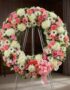 Corona fúnebre Homenaje a Jesús con rosas rosadas, claveles y crisantemos blancos, sobre un caballete en una sala de velación