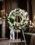 Corona fúnebre Homenaje Sincero con rosas blancas, lirios y margaritas, sobre un caballete en una sala de velación premium co