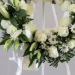 Corona fúnebre 'Homenaje Sincero' con lirios, rosas y crisantemos blancos, follaje verde, rocío sutil, cinta satinada y sobre